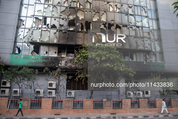 People are walking past the burnt building of the Bangladesh Bridge Authority, which students are setting on fire amid the ongoing anti-quot...