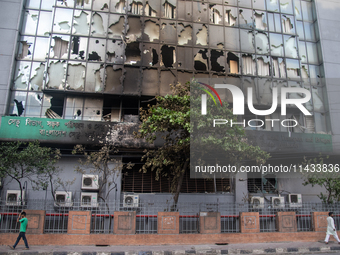 People are walking past the burnt building of the Bangladesh Bridge Authority, which students are setting on fire amid the ongoing anti-quot...