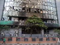 People are walking past the burnt building of the Bangladesh Bridge Authority, which students are setting on fire amid the ongoing anti-quot...