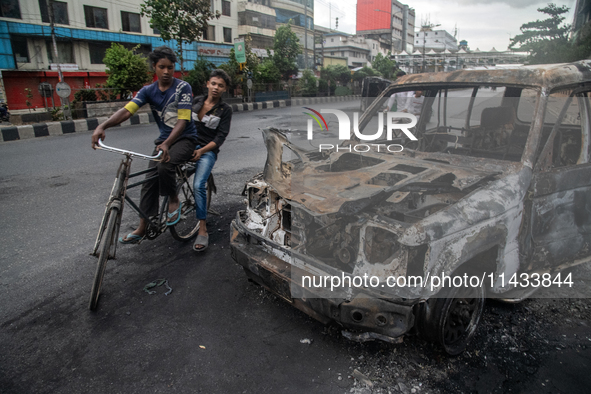 A cyclist is crossing past a burnt car on a street after students set it on fire amid the ongoing anti-quota protest in Dhaka, Bangladesh, o...