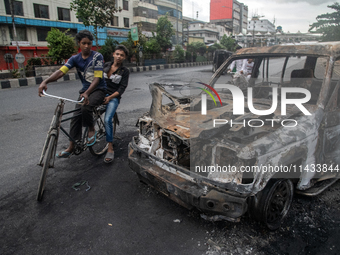 A cyclist is crossing past a burnt car on a street after students set it on fire amid the ongoing anti-quota protest in Dhaka, Bangladesh, o...