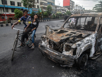 A cyclist is crossing past a burnt car on a street after students set it on fire amid the ongoing anti-quota protest in Dhaka, Bangladesh, o...