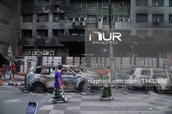 People are walking past burnt cars after students set them on fire amid the ongoing anti-quota protest in Dhaka, Bangladesh, on July 20, 202...