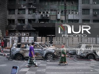 People are walking past burnt cars after students set them on fire amid the ongoing anti-quota protest in Dhaka, Bangladesh, on July 20, 202...