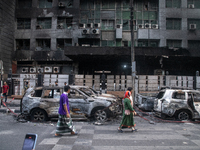 People are walking past burnt cars after students set them on fire amid the ongoing anti-quota protest in Dhaka, Bangladesh, on July 20, 202...