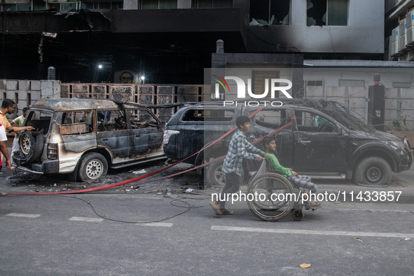 People are walking past burnt cars after students set them on fire amid the ongoing anti-quota protest in Dhaka, Bangladesh, on July 20, 202...