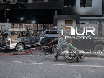 People are walking past burnt cars after students set them on fire amid the ongoing anti-quota protest in Dhaka, Bangladesh, on July 20, 202...