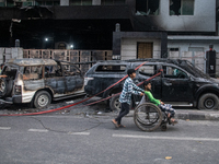 People are walking past burnt cars after students set them on fire amid the ongoing anti-quota protest in Dhaka, Bangladesh, on July 20, 202...