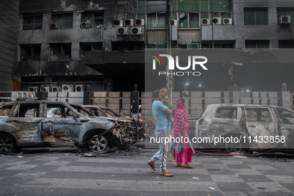 People are walking past burnt cars after students set them on fire amid the ongoing anti-quota protest in Dhaka, Bangladesh, on July 20, 202...