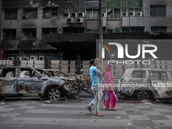 People are walking past burnt cars after students set them on fire amid the ongoing anti-quota protest in Dhaka, Bangladesh, on July 20, 202...