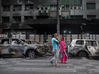 People are walking past burnt cars after students set them on fire amid the ongoing anti-quota protest in Dhaka, Bangladesh, on July 20, 202...