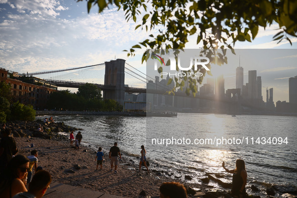  A view on Pebble Beach, Brooklyn Bridge and Manhattan skyline during sunset over the East River in New York City, United States of America...