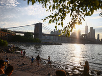  A view on Pebble Beach, Brooklyn Bridge and Manhattan skyline during sunset over the East River in New York City, United States of America...