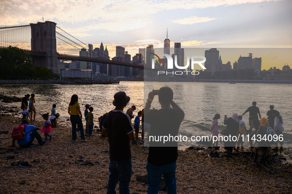  A view on Pebble Beach, Brooklyn Bridge and Manhattan skyline during sunset over the East River in New York City, United States of America...