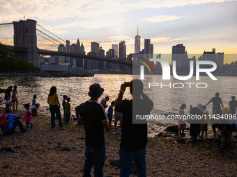  A view on Pebble Beach, Brooklyn Bridge and Manhattan skyline during sunset over the East River in New York City, United States of America...