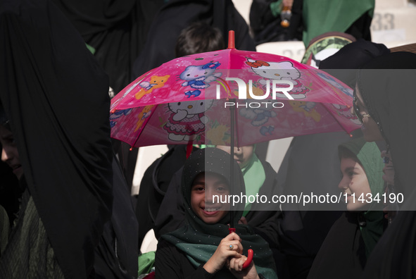 A young veiled Iranian schoolgirl is smiling as she holds a Hello Kitty umbrella while participating in a gathering to support the mandatory...