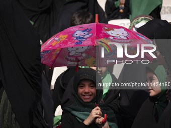 A young veiled Iranian schoolgirl is smiling as she holds a Hello Kitty umbrella while participating in a gathering to support the mandatory...