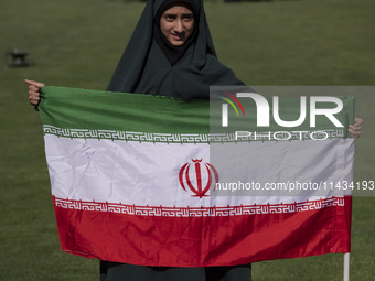 A young veiled schoolgirl is holding an Iranian flag while participating in a gathering to support the mandatory hijab at the Azadi (Freedom...