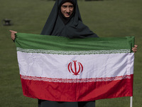 A young veiled schoolgirl is holding an Iranian flag while participating in a gathering to support the mandatory hijab at the Azadi (Freedom...