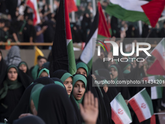 Veiled schoolgirls are holding Iranian flags and Palestinian flags while participating in a gathering to support the mandatory hijab at the...