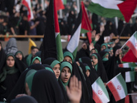 Veiled schoolgirls are holding Iranian flags and Palestinian flags while participating in a gathering to support the mandatory hijab at the...