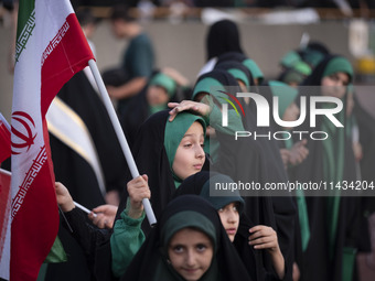 A young veiled schoolgirl is holding an Iranian flag while participating in a gathering to support the mandatory hijab at the Azadi (Freedom...