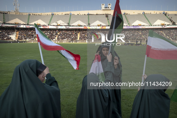 Young veiled schoolgirls are waving Iranian flags and a Palestinian flag while participating in a gathering to support mandatory hijab at th...