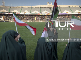 Young veiled schoolgirls are waving Iranian flags and a Palestinian flag while participating in a gathering to support mandatory hijab at th...