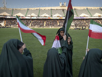 Young veiled schoolgirls are waving Iranian flags and a Palestinian flag while participating in a gathering to support mandatory hijab at th...