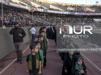 Young veiled Iranian schoolgirls and schoolboys are standing in military formation, while participating in a gathering to support mandatory...