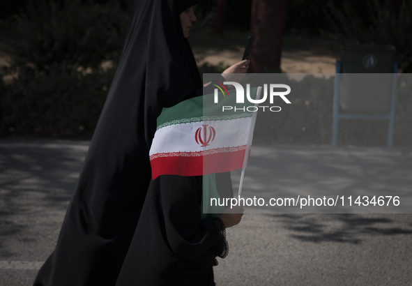 A young veiled schoolgirl is carrying an Iranian flag while walking with her mother before a family rally to support mandatory hijab, at the...