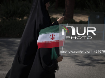 A young veiled schoolgirl is carrying an Iranian flag while walking with her mother before a family rally to support mandatory hijab, at the...