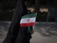 A young veiled schoolgirl is carrying an Iranian flag while walking with her mother before a family rally to support mandatory hijab, at the...