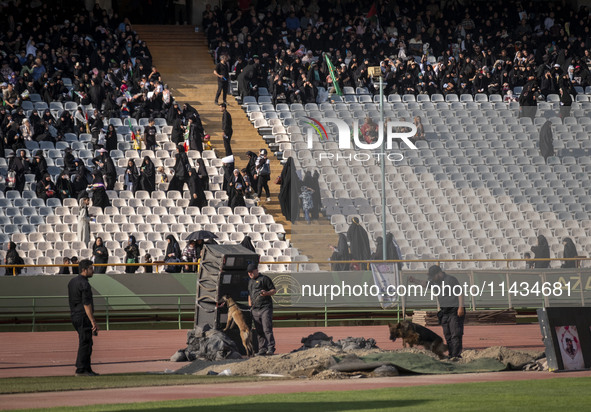 Two security personnel are searching an area with dogs before the beginning of a family rally to support mandatory hijab, at the Azadi (Free...