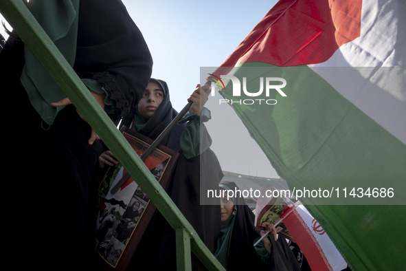 Young veiled women are carrying an Iranian flag and a Palestinian flag while participating in a family rally to support mandatory hijab, in...