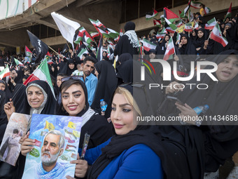 Two young Iranian women are sitting next to their veiled mother while holding a poster featuring a portrait of former commander of the Islam...