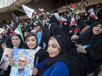 Two young Iranian women are sitting next to their veiled mother while holding a poster featuring a portrait of former commander of the Islam...