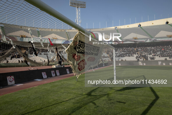 A religious flag and headbands are hanging and tied on a soccer goal, while veiled Iranian women are participating in a family rally to supp...