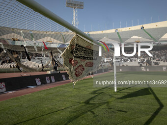 A religious flag and headbands are hanging and tied on a soccer goal, while veiled Iranian women are participating in a family rally to supp...