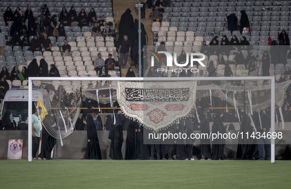 A religious flag is hanging on a soccer goal, while veiled Iranian women are participating in a family rally to support mandatory hijab, at...