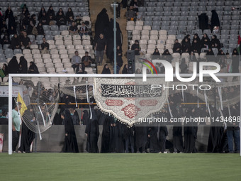 A religious flag is hanging on a soccer goal, while veiled Iranian women are participating in a family rally to support mandatory hijab, at...