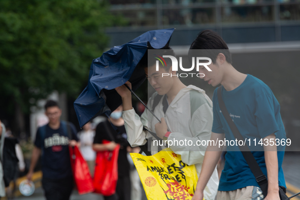 People are trying to hold umbrellas in a big wind in front of the International Expo Center in Shanghai, China, on July 26, 2024. 