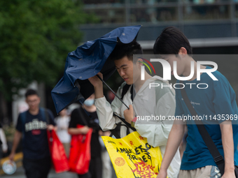 People are trying to hold umbrellas in a big wind in front of the International Expo Center in Shanghai, China, on July 26, 2024. (