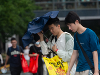 People are trying to hold umbrellas in a big wind in front of the International Expo Center in Shanghai, China, on July 26, 2024. (