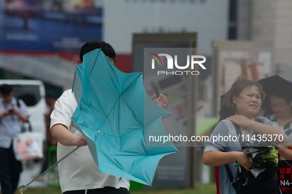 People are trying to hold umbrellas in a big wind in front of the International Expo Center in Shanghai, China, on July 26, 2024. 