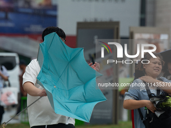 People are trying to hold umbrellas in a big wind in front of the International Expo Center in Shanghai, China, on July 26, 2024. (