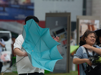 People are trying to hold umbrellas in a big wind in front of the International Expo Center in Shanghai, China, on July 26, 2024. (