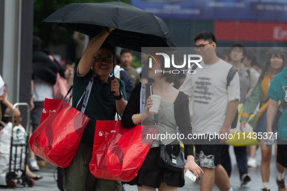 People are trying to hold umbrellas in a big wind in front of the International Expo Center in Shanghai, China, on July 26, 2024. 