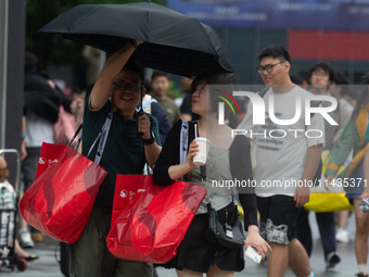 People are trying to hold umbrellas in a big wind in front of the International Expo Center in Shanghai, China, on July 26, 2024. (