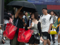 People are trying to hold umbrellas in a big wind in front of the International Expo Center in Shanghai, China, on July 26, 2024. (